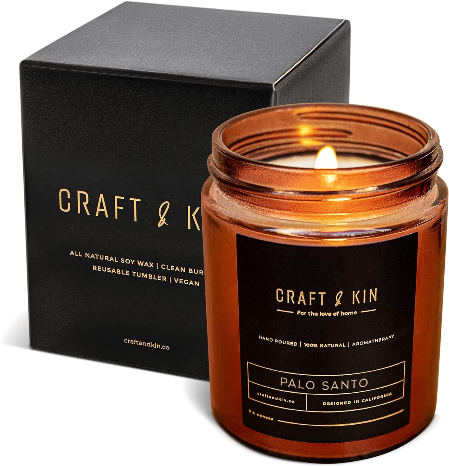 Amber glass candle jar labeled 'Craft & Kin - Palo Santo,' with a lit flame, placed next to its matching black gift box. The box features elegant gold text highlighting the brand and product details. A luxurious and minimal design, perfect for creating a warm and soothing ambiance.